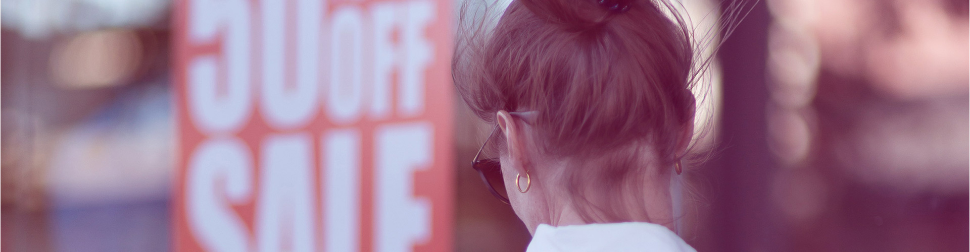 Blog banner featuring back of woman's head as she looks at 50% off sale sign on window
