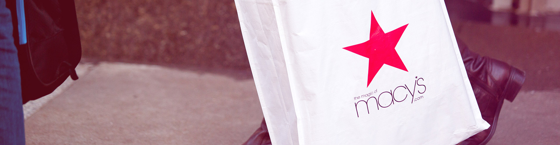 Macy’s Plan to Build Private Label Brands Faces Tough Odds blog banner featuring close up of a Macy's shopping bag a woman in boots is carrying
