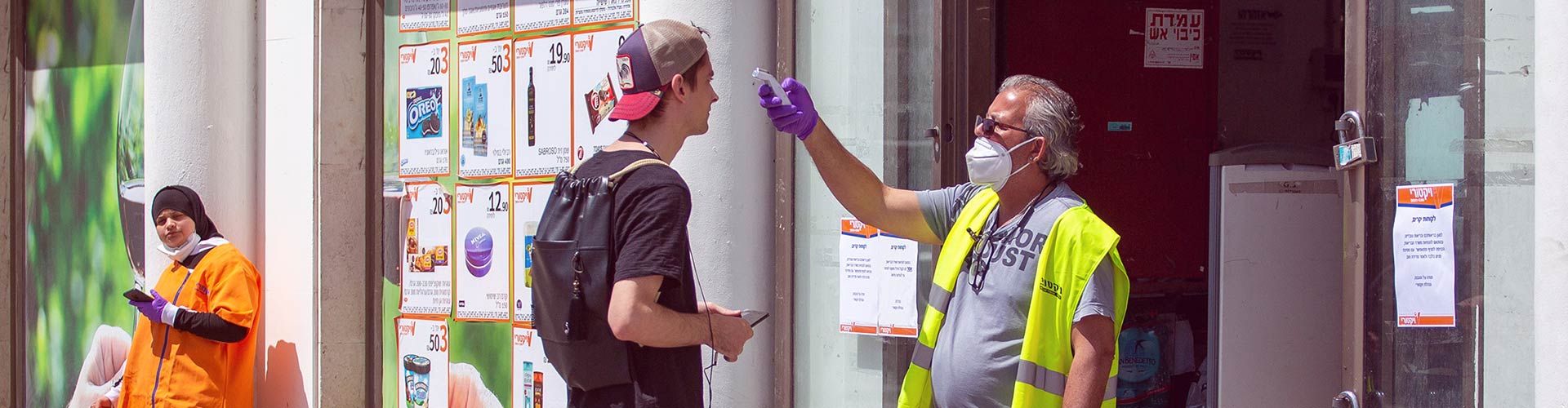 Retail Safari® Reopened Retail: A Look at Israel blog banner featuring man with a face mask temperature checking a young man trying to enter a building