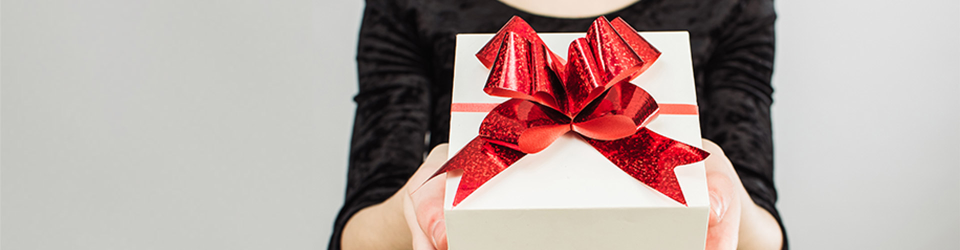WSL COVID Holiday Gifting - In The Words of Shoppers Banner featuring person in black shirt handing someone a gift with a red bow