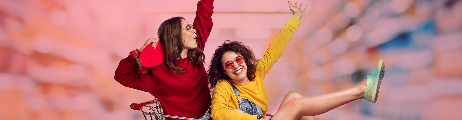 Two Gen Z teens having fun rolling around in a shopping cart - banner